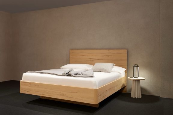 Ein modernes, minimalistisches Bett mit hellen Holzdetails und Kissen.