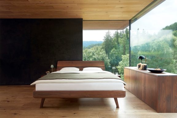 Modern Schlafzimmer mit Holzbetten, großen Fenstern und Blick auf die Natur.