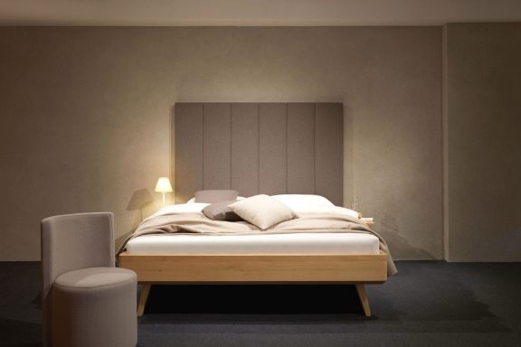 Minimalistisch eingerichtetes Schlafzimmer mit Bett, Kissen und einem Stuhl.